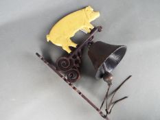 A wall mountable, cast iron bell surmounted with a depiction of a pig.