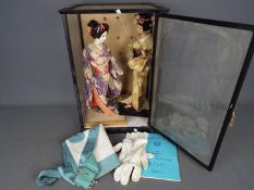 Two dolls in traditional Japanese dress contained in a display case approximately 49 cm x 33 cm x