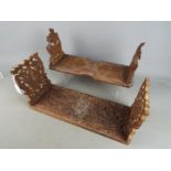 Two carved wooden, sliding book racks, the ends with carved foliate motifs.