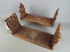 Two carved wooden, sliding book racks, the ends with carved foliate motifs.