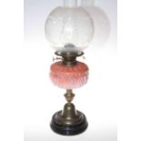 Brass oil lamp with pink glass reservoir and frosted glass shade.