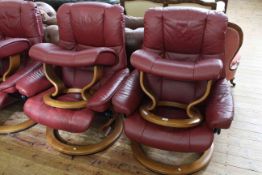 Pair Ekornes Stressless burgundy leather adjustable swivel chairs and footstools.