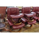 Pair Ekornes Stressless burgundy leather adjustable swivel chairs and footstools.