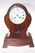 Shaped mahogany mantel clock raised on bracket feet with enamelled and Roman numeral dial,