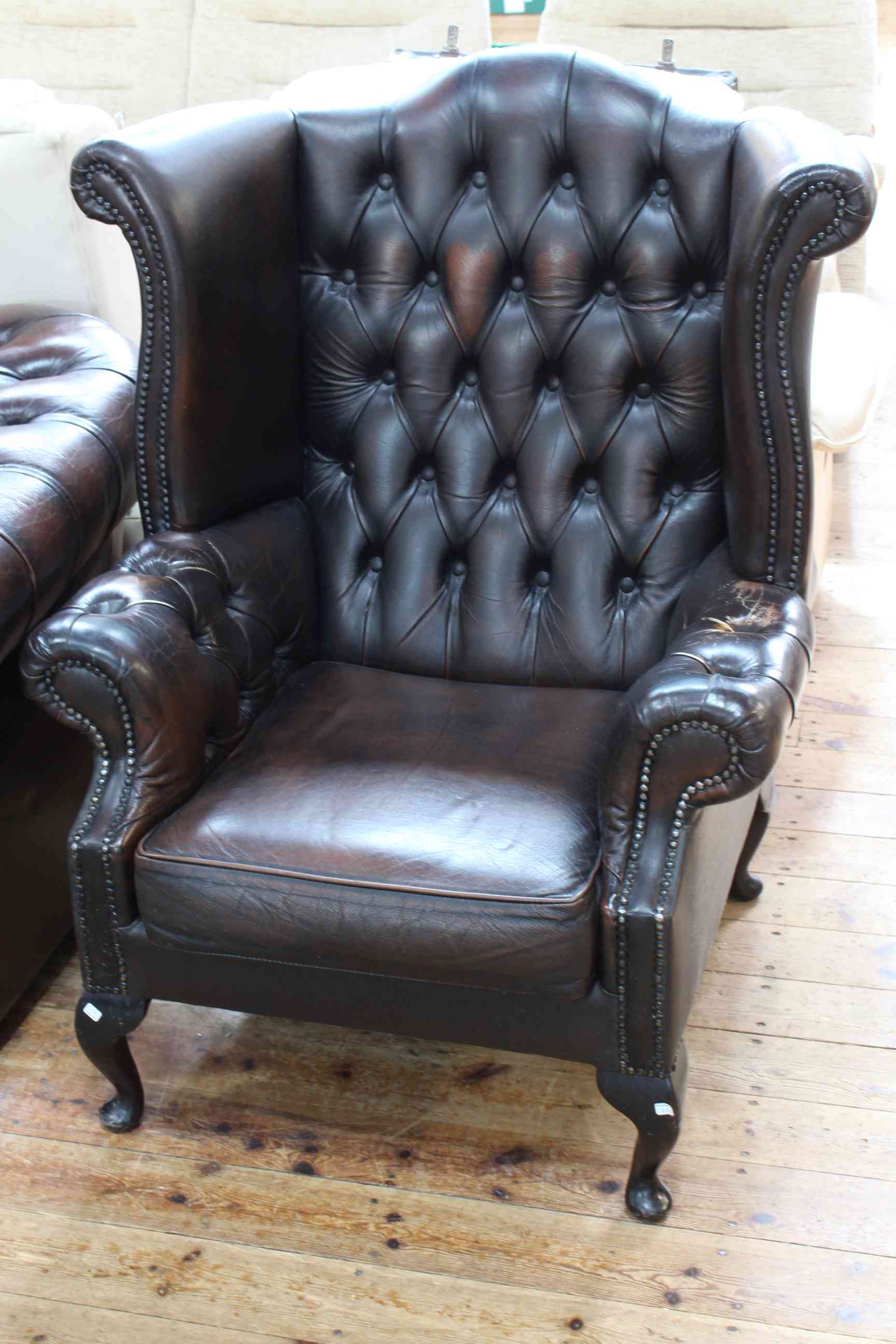 Brown buttoned leather and studded wing back armchair on cabriole legs.