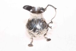 George III silver pot bellied cream jug with embossed decoration and on three shaped legs,