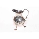 George III silver pot bellied cream jug with embossed decoration and on three shaped legs,