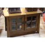 Sherry medium oak entertainment unit in Arts & Crafts style having two glazed panel doors,