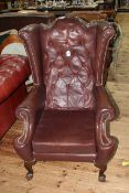 Brown buttoned leather and studded wing armchair on ball and claw legs.
