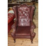 Brown buttoned leather and studded wing armchair on ball and claw legs.