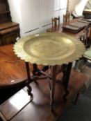 An ornate brass topped table on a folding wooden base,