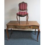 A French walnut three drawer writing table and a chair in striped fabric