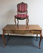 A French walnut three drawer writing table and a chair in striped fabric