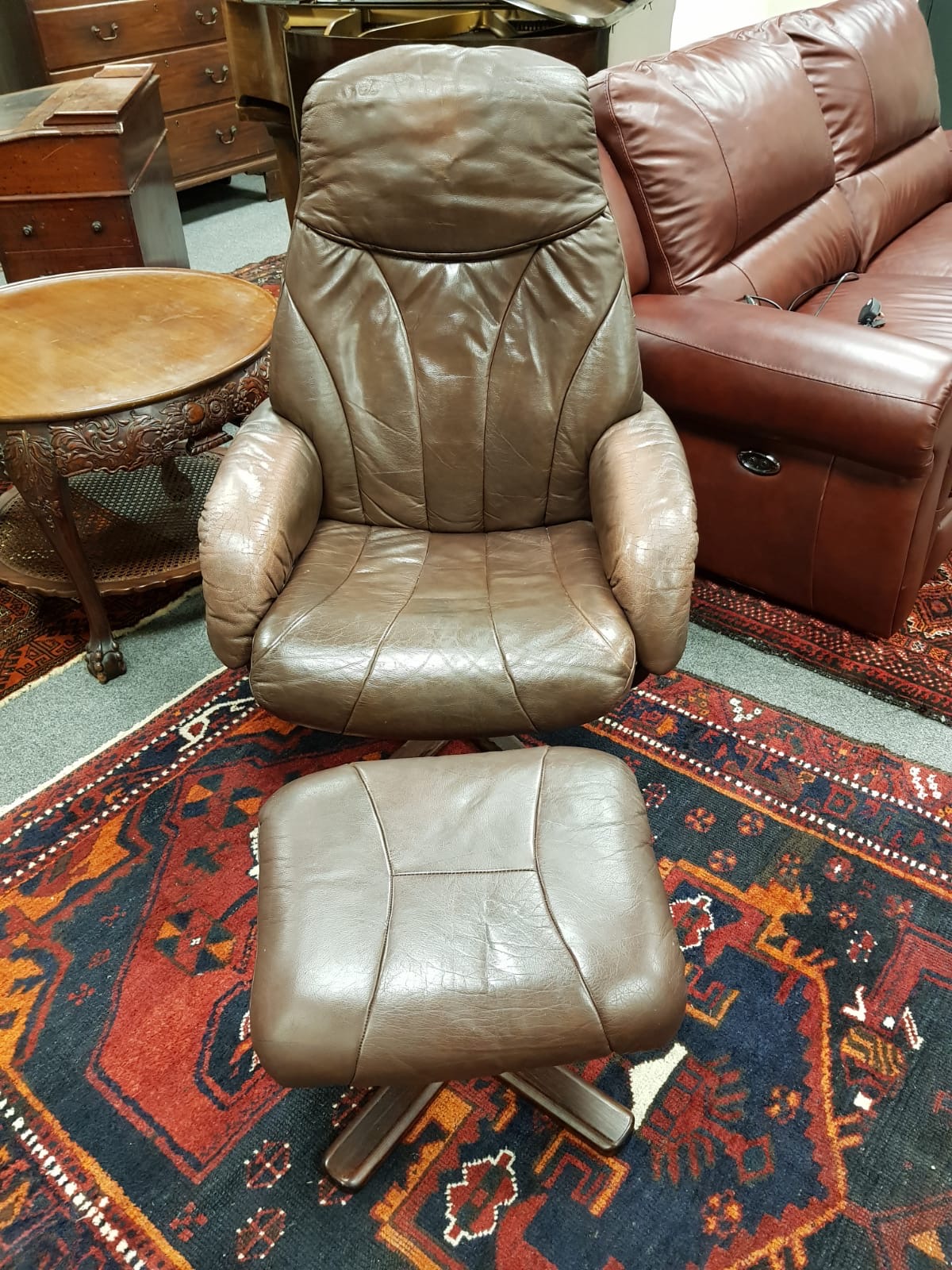 A brown leather swivel relaxer chair with stool, 77 cm width.