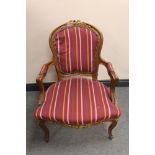 A carved French walnut and gilt salon armchair in striped fabric