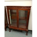 A reproduction mahogany glazed double door cabinet on claw and ball feet,