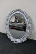 An ornate silvered oval framed mirror