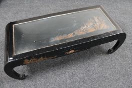 A carved hardwood Chinese coffee table with glass top depicting figures at a temple