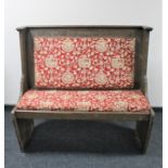 A carved oak pew in red heraldic upholstery