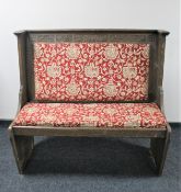 A carved oak pew in red heraldic upholstery