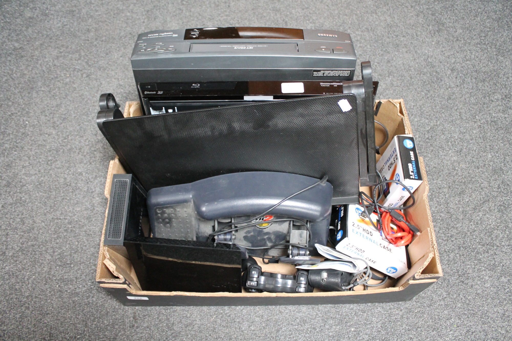 A box of Samsung VCR, Sony blu-ray player with remote, routers, third party playstation controller,