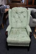 A stained beech framed wing armchair in green buttoned fabric
