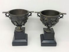 A pair of cast bronze urns on slate pedestals,