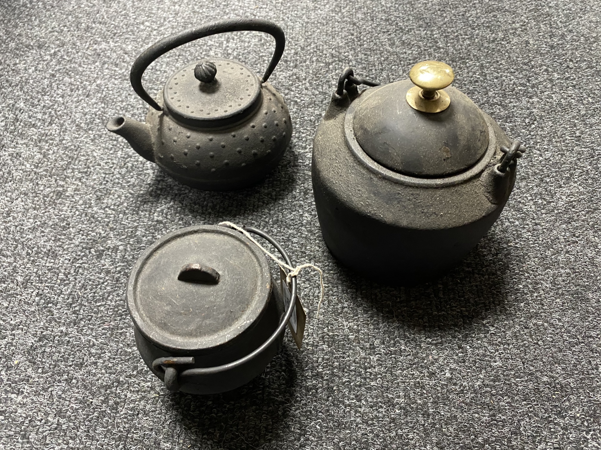 Two miniature cast iron cooking pots with lids together with a cast iron kettle with lid