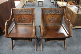 A pair of Edwardian heavily carved oak library chairs on X-frame supports.