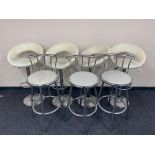 A set of four metal based gas lift bar stools upholstered in a cream faux leather fabric,