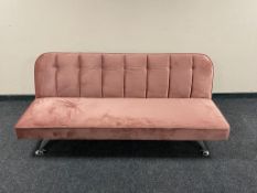 A contemporary folding bed settee in pink fabric on metal legs