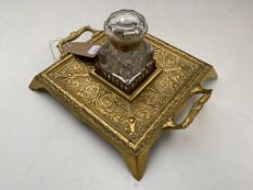 A Victorian brass twin handled embossed desk stand on raised feet with glass inkwell