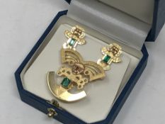 An 18ct gold matching brooch and earring set in Aztec style set with emeralds