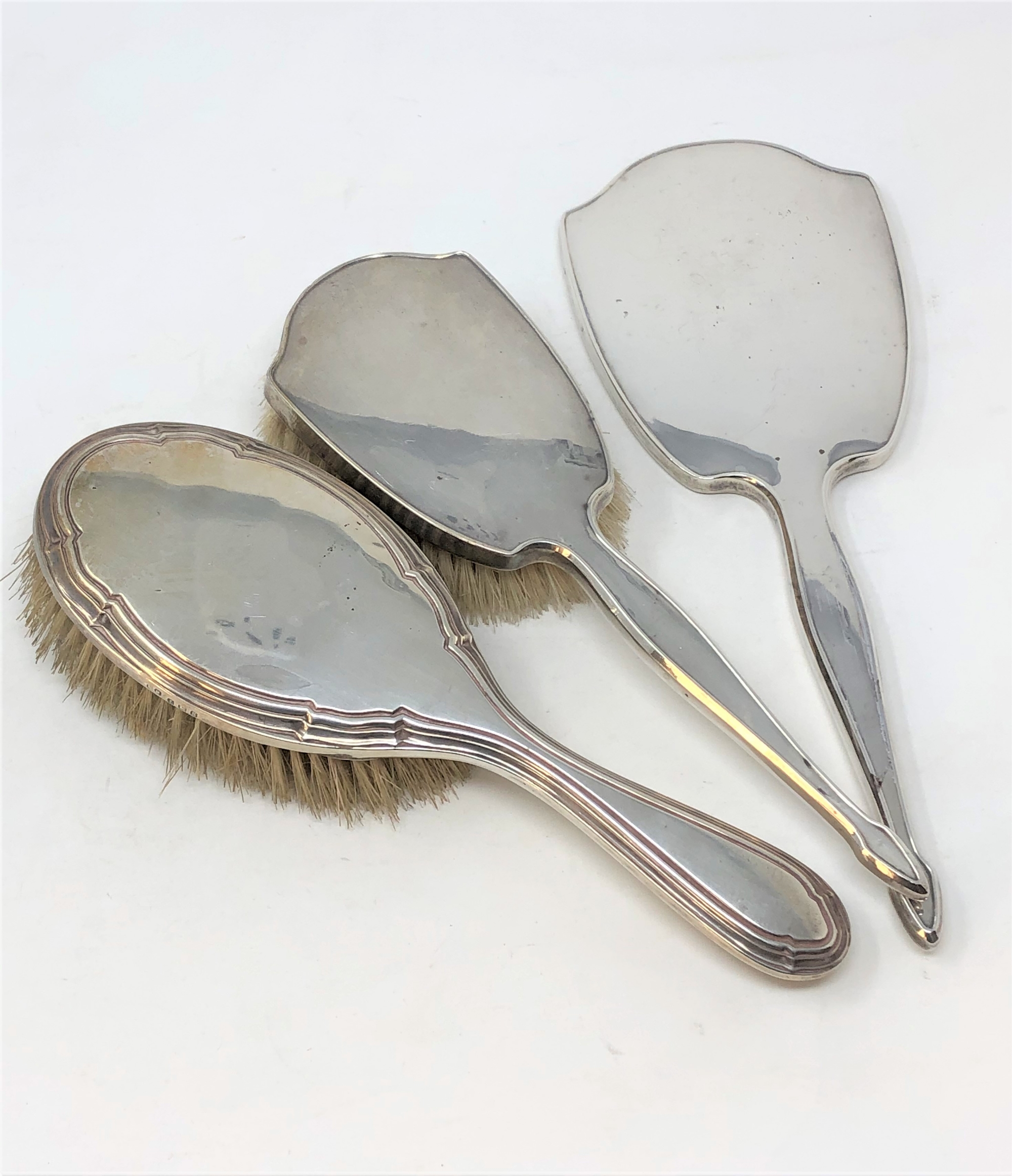 A silver hand mirror, matching brush and another non-matching silver brush.