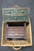 A wicker twin handled log basket containing a hardwood painted three drawer chest and an Edwardian