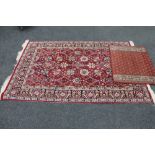 A fringed floral rug on red ground together with a further mat