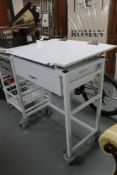 A metal medical trolley with adjustable top fitted a drawer