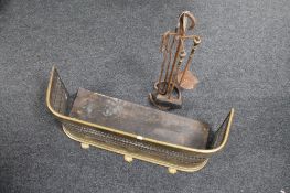 An antique brass fender together with a cast iron three piece companion set on stand