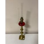 An antique Kosmos Brenner brass and cranberry glass oil lamp with chimney on brass base