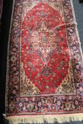 A fringed Iranian rug on red ground 91 cm x 179 cm.