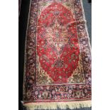 A fringed Iranian rug on red ground 91 cm x 179 cm.