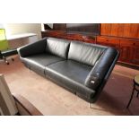 A shaped black leather two seater settee on metal legs