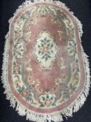 An oval Chinese floral fringed rug on pink ground.