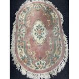 An oval Chinese floral fringed rug on pink ground.