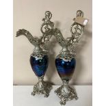 A pair of white metal and petrol glass ewers