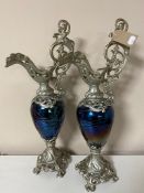 A pair of white metal and petrol glass ewers