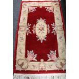 A fringed Chinese floral rug on red ground
