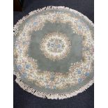 A circular Chinese floral fringed rug on green ground.
