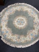 A circular Chinese floral fringed rug on green ground.