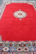 A fringed woolen Persian carpet on red ground with central medallion 440 cm x 295 cm.